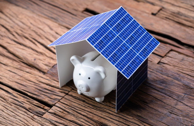 Cochon tirelire sous une maison en panneau solaire