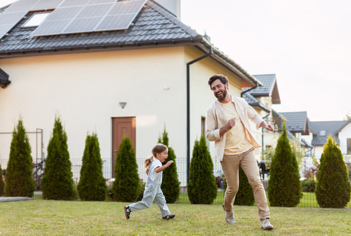Maison équipée de panneaux solaires avec un père et sa fille dans le jardin.