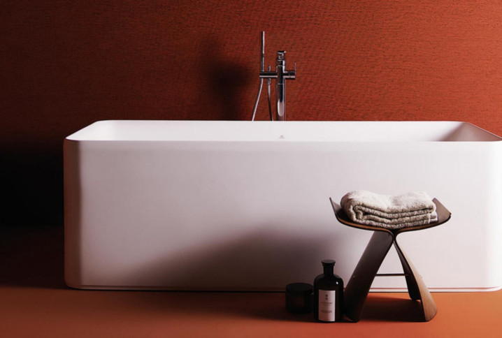 Baignoire îlot blanche rectangulaire aux lignes épurées dans une salle de bains aux tons terracotta.