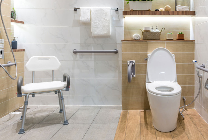 salle de bains accessible aux PMR avec toilettes et barre d'appui avec carrelage antidérapant au sol et siège de douche sécurisé