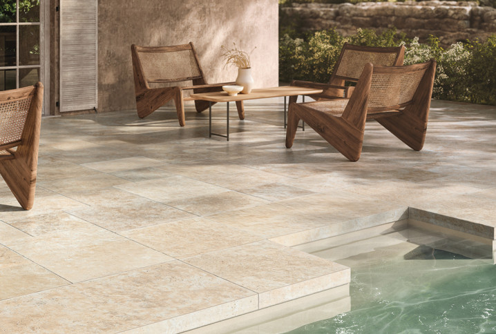 Terrasse extérieure en carrelage effet pierre beige autour d’une piscine avec mobilier en bois naturel.