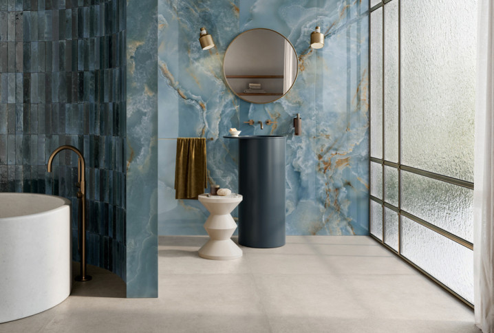 Salle de bains élégante avec carrelage mural effet marbre bleu, baignoire îlot blanche et vasque sur colonne bleu foncé.