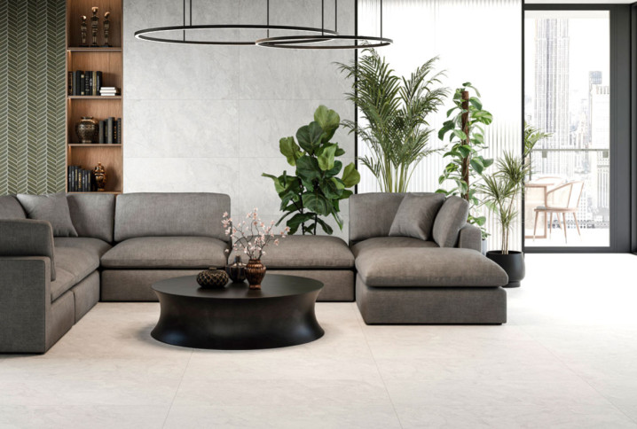 Salon contemporain avec grand canapé d’angle gris, table basse noire et carrelage grand format beige clair au sol.