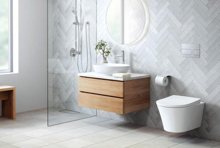 Salle de bains lumineuse avec WC suspendu blanc, meuble vasque en bois et carrelage mural en chevrons.