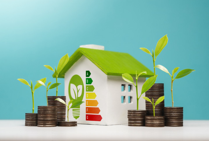 Petite maison à toit vert avec étiquette énergie et piles de pièces, symbolisant les économies d’énergie.