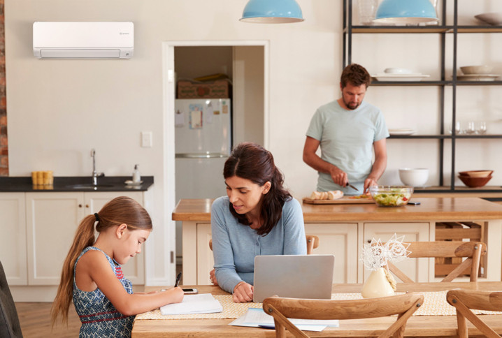 cuisine moderne où une femme travaille sur un ordinateur portable avec un enfant et un homme cuisine en arrière-plan avec un climatiseur mural