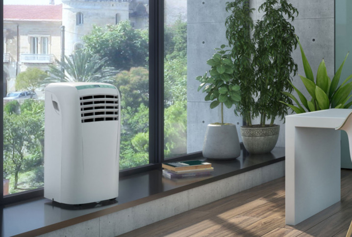 Climatiseur mobile blanc installé près d’une baie vitrée dans un intérieur moderne et lumineux.