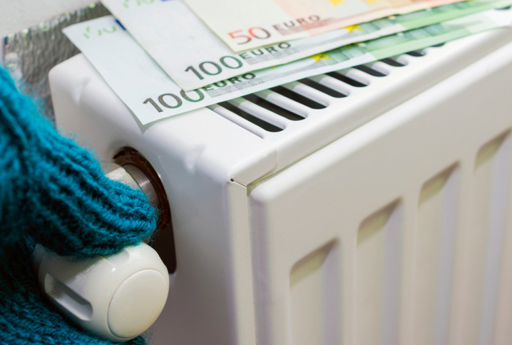 Personne avec des gants qui règle la température d'un radiateur sur lequel est posé des billets de 100 et 50 euros