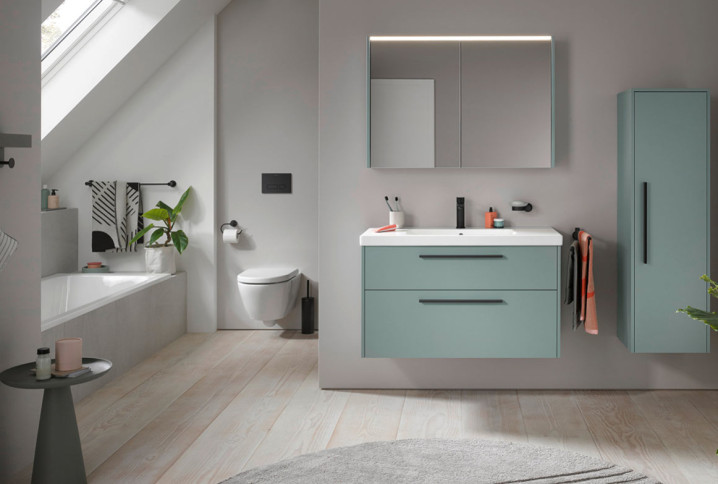 Meuble vasque suspendu vert avec deux tiroirs, miroir lumineux et colonne de rangement assortie.