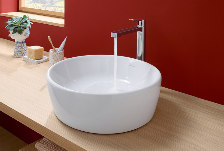 Vasque à poser installée sur un meuble de salle de bains en bois, eau qui coule du robinet