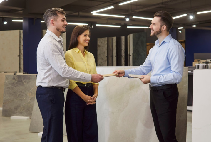 Trois personnes dans un magasin spécialisé en carrelage, un homme remet un carreau de carrelage à un couple