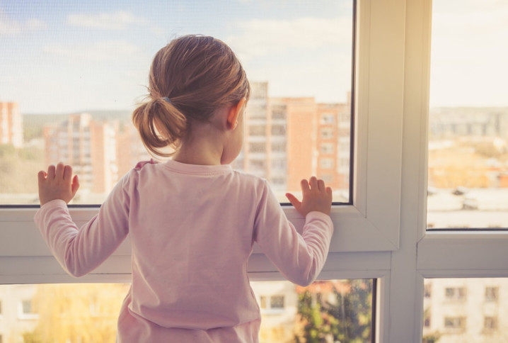 Petite fille qui regarde par la fenêtre d'un immeuble