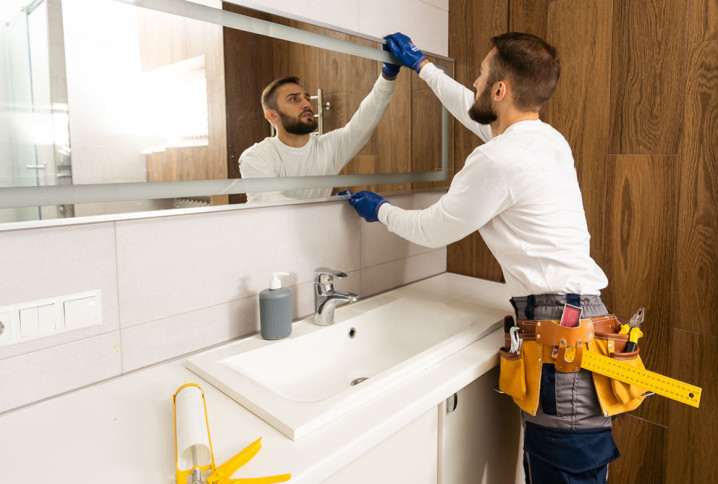 Artisan prenant les mesures d’un meuble vasque avant son démontage dans une salle de bains.