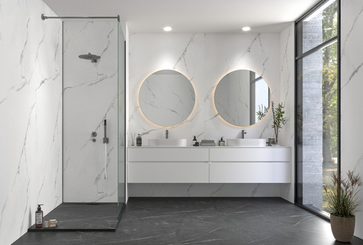 Salle de bains moderne avec douche à l’italienne, double vasque suspendue et grands carreaux effet marbre blanc.
