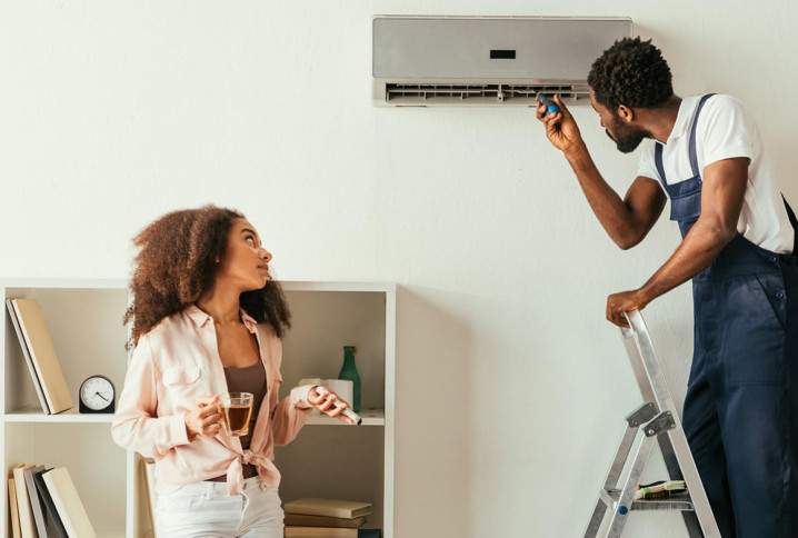 homme sur une échelle inspecte un climatiseur mural blanc avec un outil et une femme le regarde