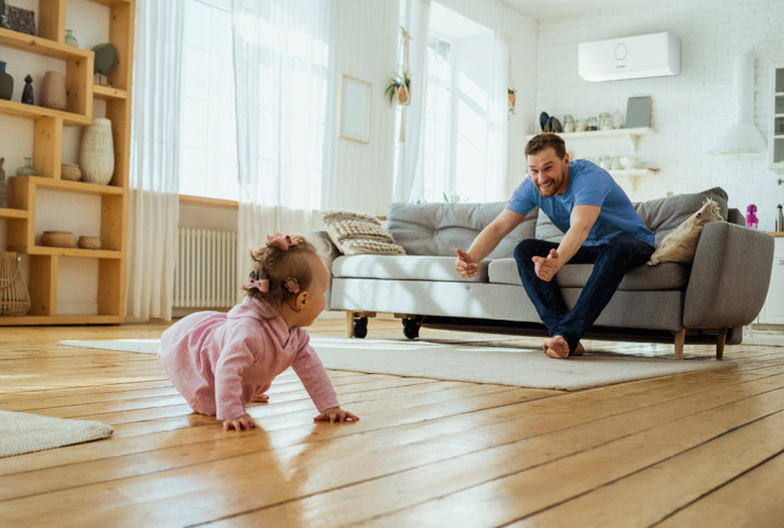 Famille profitant d’un salon climatisé avec un bébé jouant sur le parquet en bois.