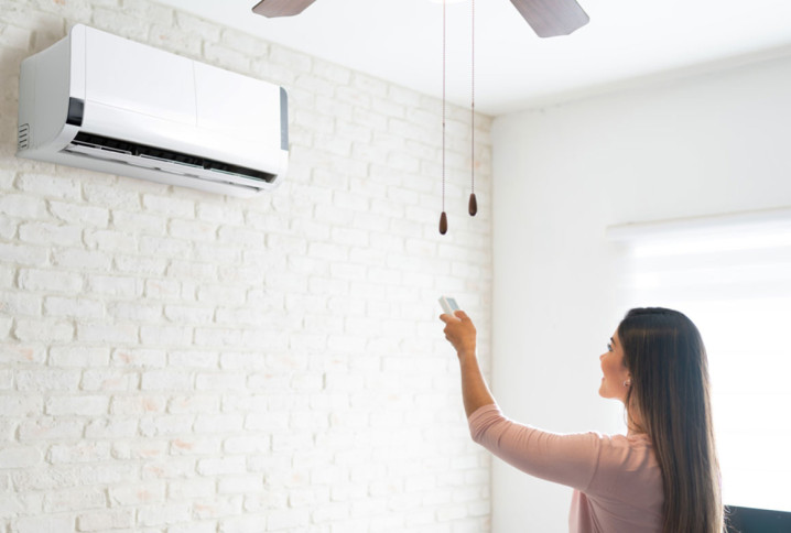  femme vue de dos utilise une télécommande pour régler un climatiseur mural blanc dans une pièce lumineuse