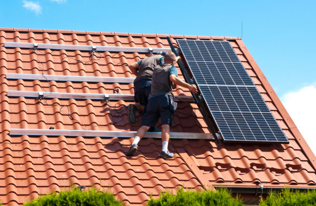 Personne qui fixe des panneaux solaires sur des tuiles romanes