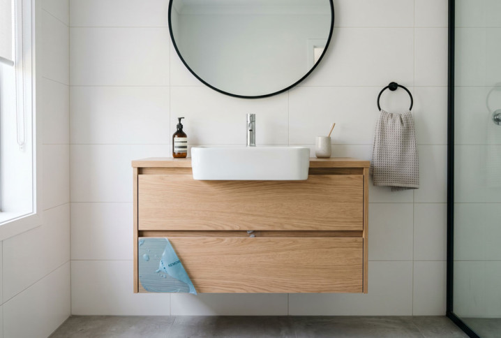 Meuble de salle de bains suspendu en bois avec vasque à poser et grand miroir rond.