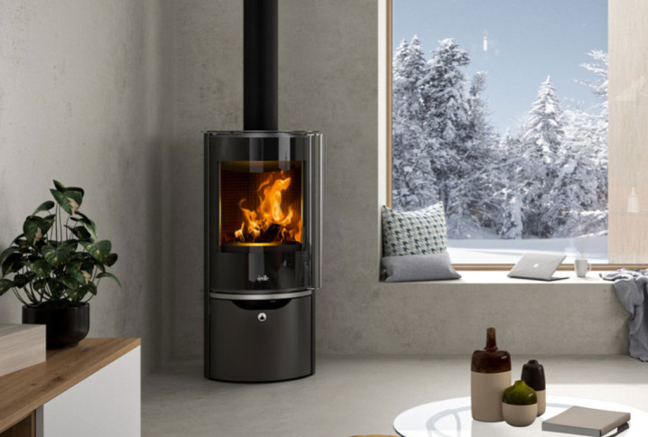 Poêle à bois noir installé dans le coin d'une pièce de maison, temps hivernal visible par la fenêtre