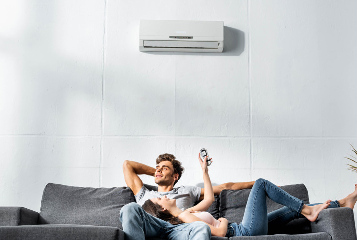 Couple détendu sur un canapé sous un climatiseur mural, contrôlant la température avec une télécommande.