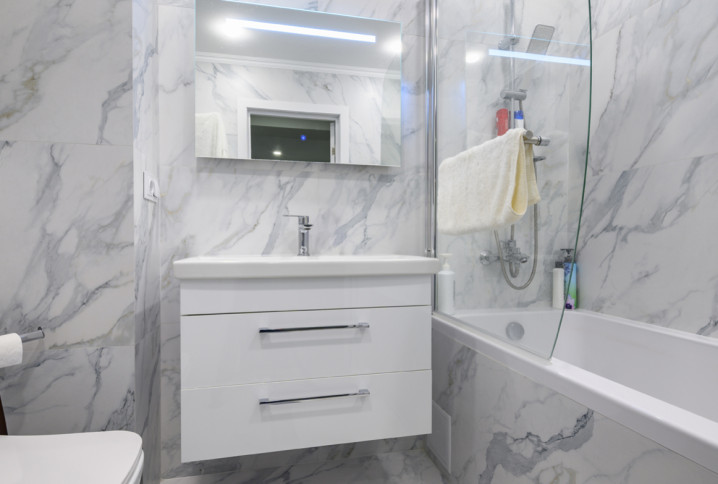Petite salle de bains rénovée avec carrelage effet marbre, meuble suspendu blanc et baignoire moderne.