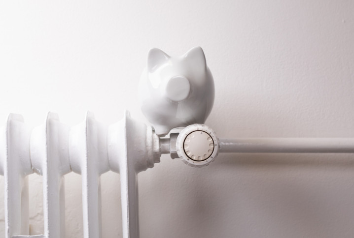 Radiateur blanc avec robinet thermostatique et tirelire posée au-dessus pour illustrer les économies de chauffage.