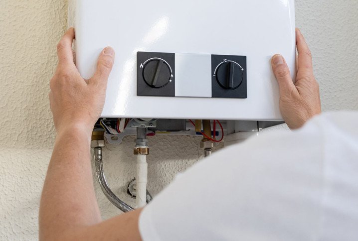 Technicien intervenant sur une chaudière murale à gaz pour contrôler ses branchements et son fonctionnement.
