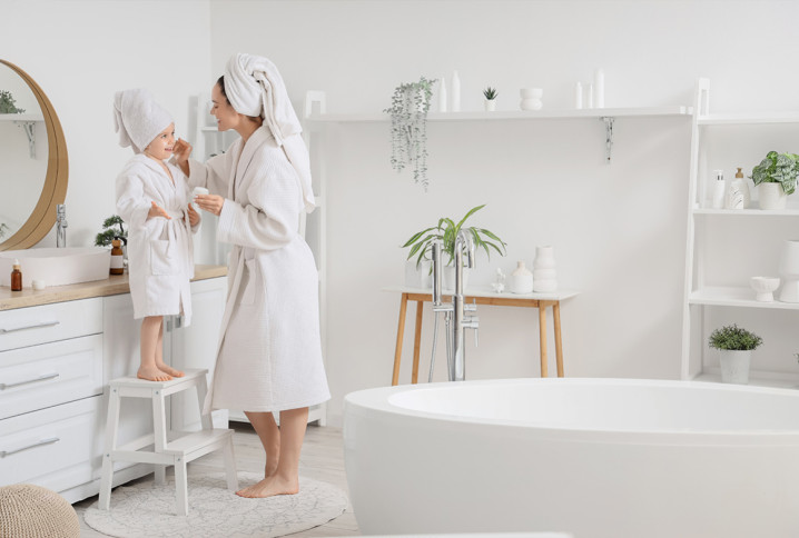 Mère et enfant en peignoir dans une salle de bains familiale lumineuse avec baignoire îlot et meuble vasque.