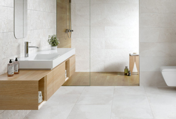 Salle de bains minimaliste avec meuble suspendu en bois clair, douche à l’italienne et WC suspendu.