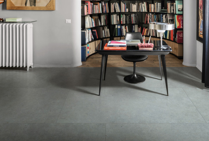 Sol en grès cérame gris grand format dans un bureau, ambiance contemporaine avec bibliothèque et radiateur design.