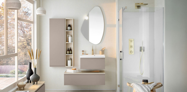 Salle de bains lumineuse avec meuble vasque beige suspendu, colonne de rangement murale, miroir asymétrique et cabine de douche vitrée.