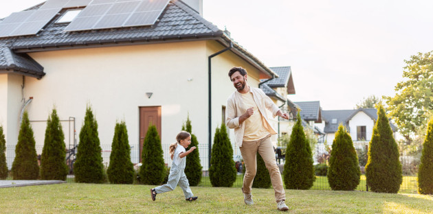 Maison équipée de panneaux solaires avec un père et sa fille dans le jardin.