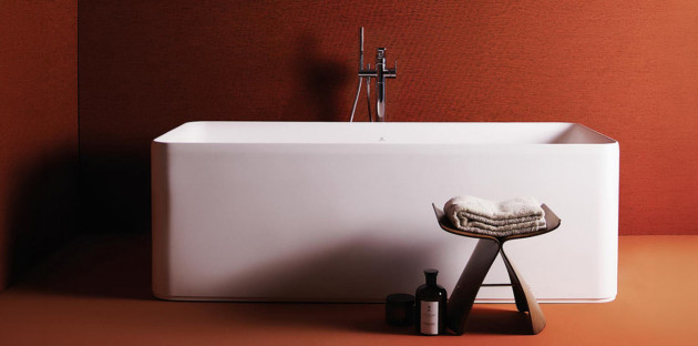 Baignoire îlot blanche rectangulaire aux lignes épurées dans une salle de bains aux tons terracotta.