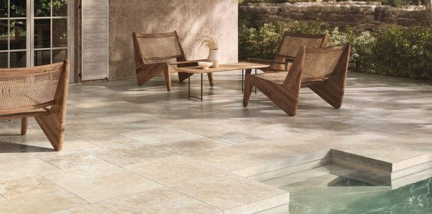Terrasse extérieure en carrelage effet pierre beige autour d’une piscine avec mobilier en bois naturel.