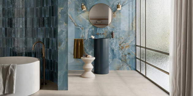 Salle de bains élégante avec carrelage mural effet marbre bleu, baignoire îlot blanche et vasque sur colonne bleu foncé.
