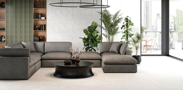 Salon contemporain avec grand canapé d’angle gris, table basse noire et carrelage grand format beige clair au sol.