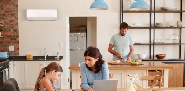 cuisine moderne où une femme travaille sur un ordinateur portable avec un enfant et un homme cuisine en arrière-plan avec un climatiseur mural