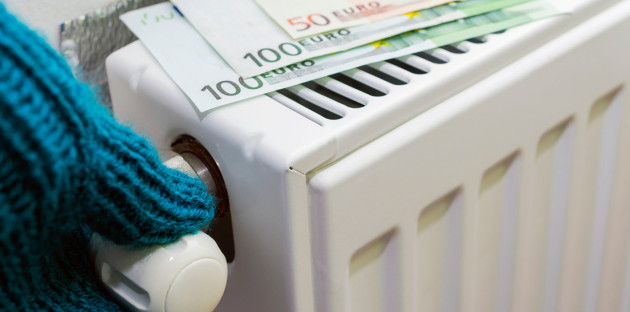 Personne avec des gants qui règle la température d'un radiateur sur lequel est posé des billets de 100 et 50 euros