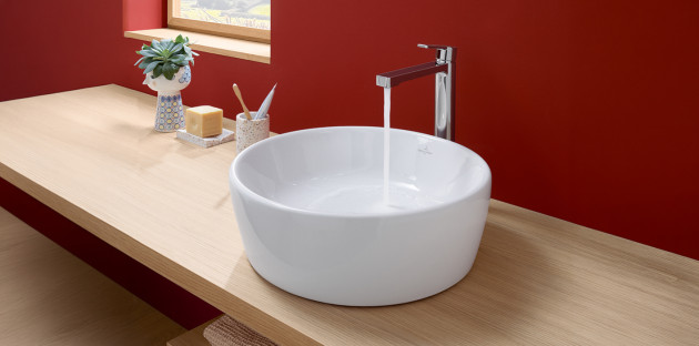 Vasque à poser installée sur un meuble de salle de bains en bois, eau qui coule du robinet