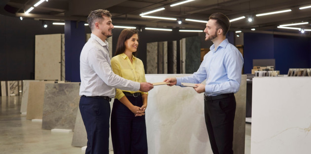 Trois personnes dans un magasin spécialisé en carrelage, un homme remet un carreau de carrelage à un couple