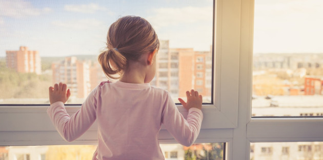 Petite fille qui regarde par la fenêtre d'un immeuble