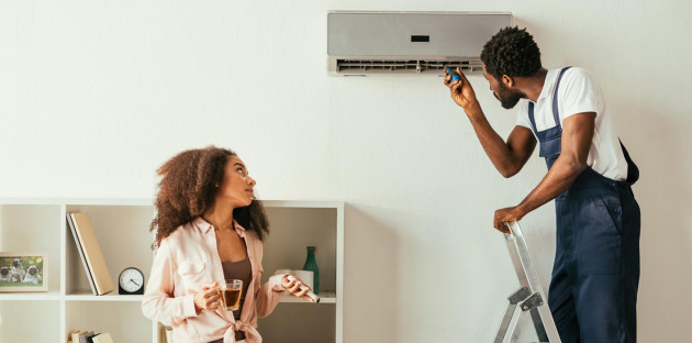 homme sur une échelle inspecte un climatiseur mural blanc avec un outil et une femme le regarde