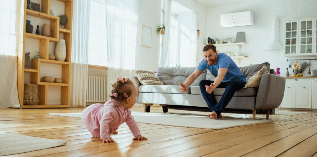 Famille profitant d’un salon climatisé avec un bébé jouant sur le parquet en bois.