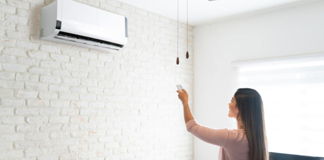 femme qui utilise une télécommande pour régler un climatiseur mural blanc dans une pièce lumineuse