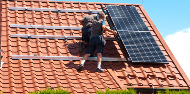 Personne qui fixe des panneaux solaires sur des tuiles romanes