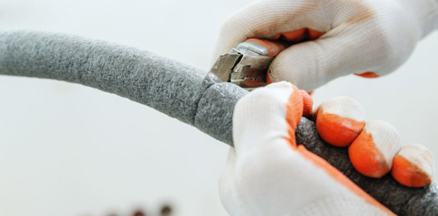 Homme avec des gants qui utilise un cutter pour découper un tuyau