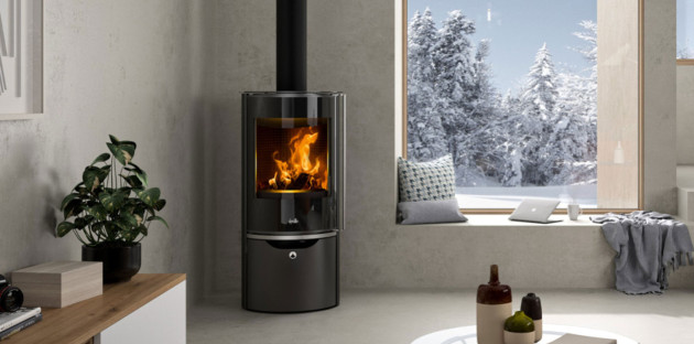 Poêle à bois noir installé dans le coin d'une pièce de maison, temps hivernal visible par la fenêtre