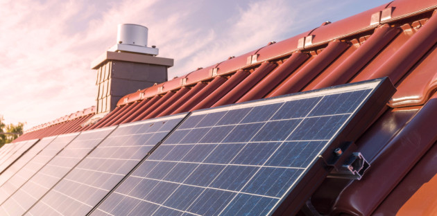 Panneaux solaires photovoltaïques installés sur une toiture en tuiles rouges, éclairés par le soleil.