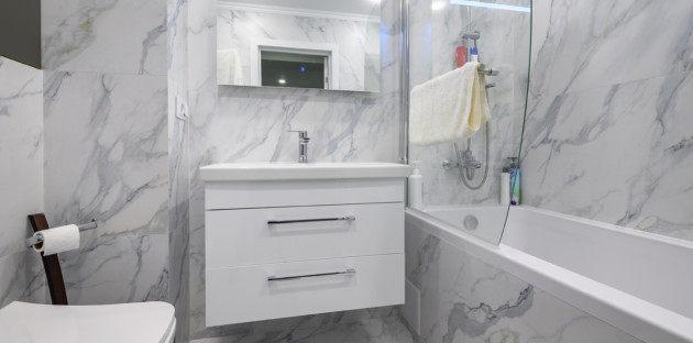 Petite salle de bains rénovée avec carrelage effet marbre, meuble suspendu blanc et baignoire moderne.